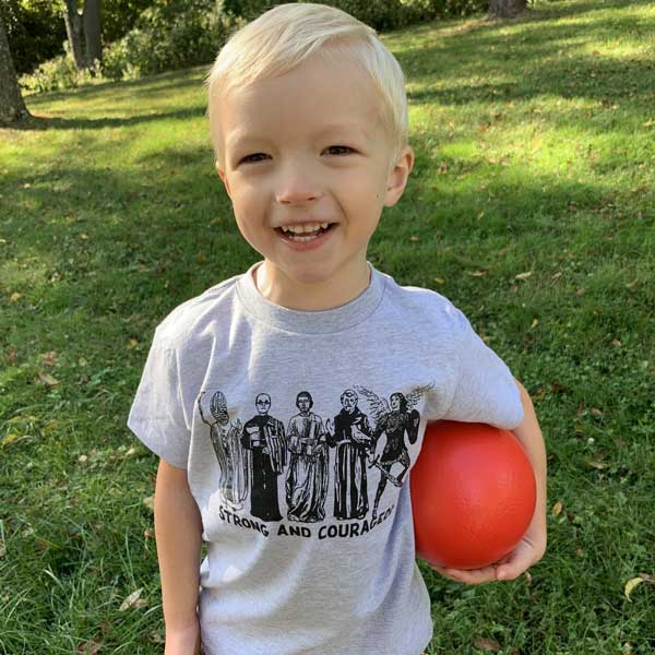 Young boy wearing Strong and Courageous grey tee with a red ball in a park setting