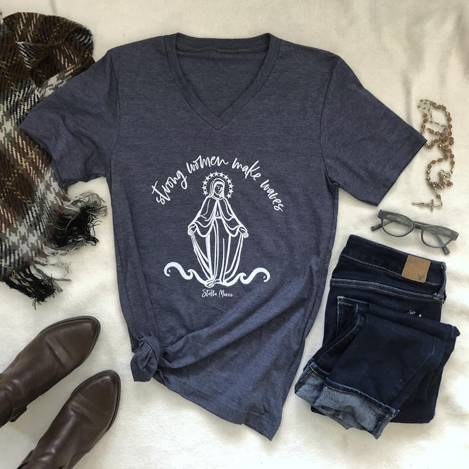 Navy v-neck 'Strong Women Make Waves' tee with illustration, styled with jeans and accessories on a white background.