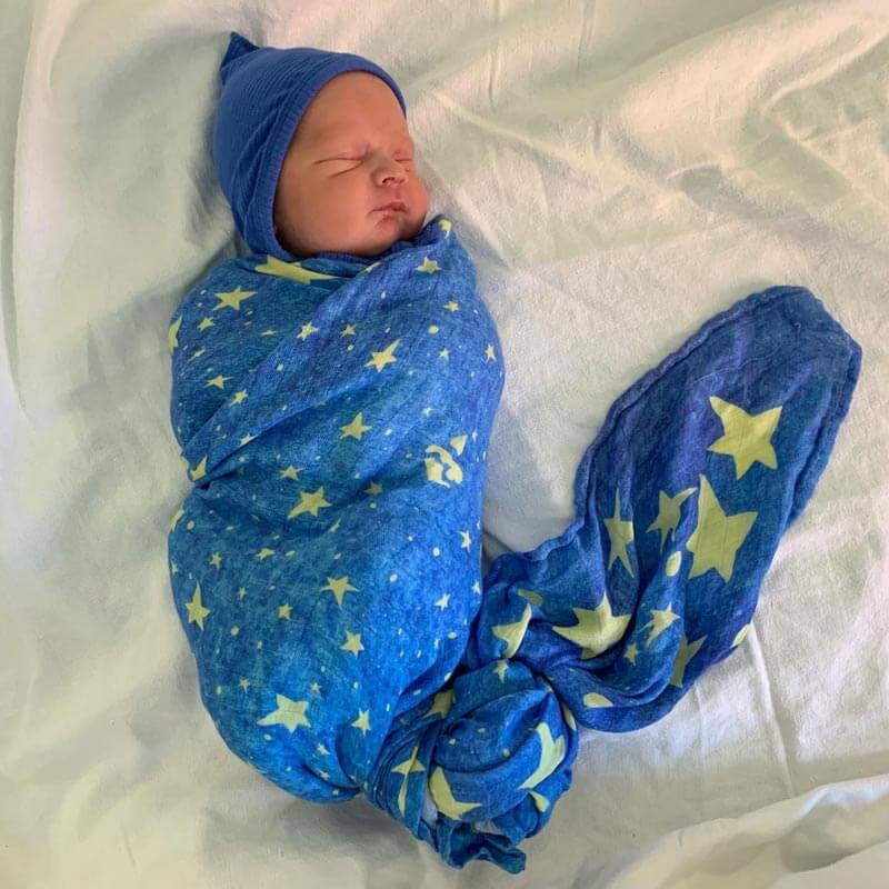 Newborn baby wrapped in a star-patterned blue Mary's Mantle Swaddle, symbolizing protection and comfort.